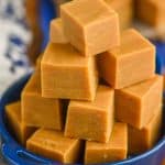 a pyramid of peanut butter fudge piled into a small blue dish with handles on a white napkin and a wood block
