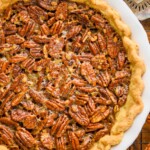 overhead view of a full pecan pie recipe in a white ceramic pie plate with an antique pie server next to it and sitting on a wire rack - 9