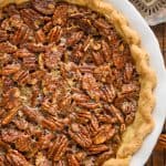overhead view of a full pecan pie recipe in a white ceramic pie plate with an antique pie server next to it and sitting on a wire rack