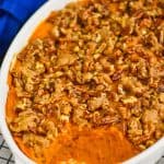 side view of a sweet potato casserole that is topped with pecans that has some of the dish scooped out, sitting on a wire cooling rack