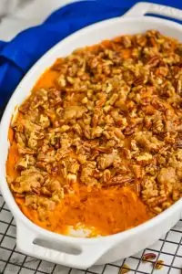 side view of a sweet potato casserole that is topped with pecans that has some of the dish scooped out, sitting on a wire cooling rack