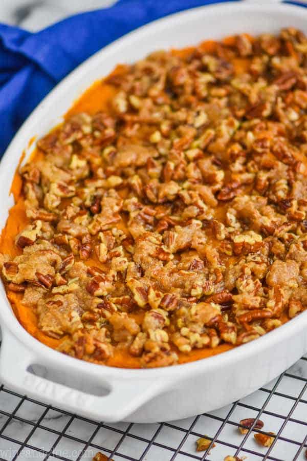 sweet potato casserole with pecans in a white casserole dish on a wire rack with a blue towel in the background