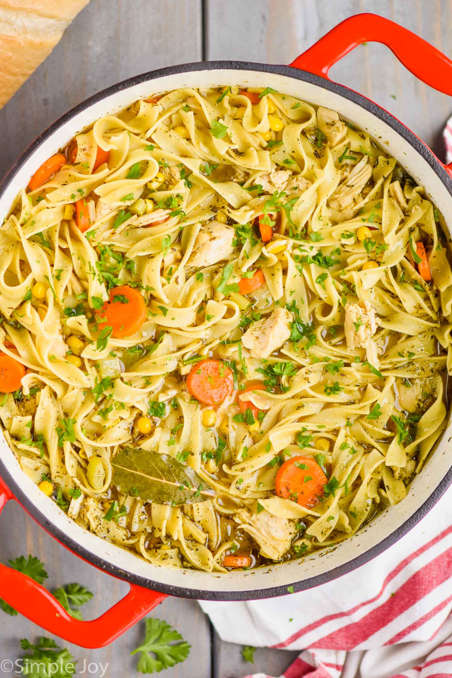 overhead view of a red handled stock pot full of turkey noodle soup - long noodles, pieces of turkey, a bay leaf, carrots, and corn are visible - 3