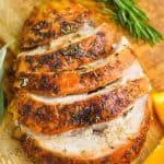 turkey breast that has been cooked and is cut up sitting on a cutting board with orange slices and rosemary sprigs