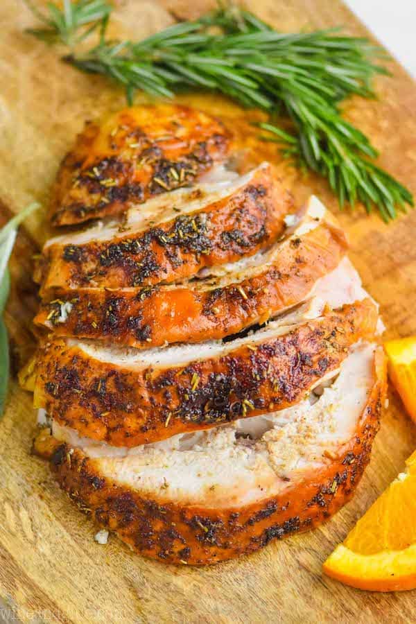 turkey breast that has been cooked and is cut up sitting on a cutting board with orange slices and rosemary sprigs