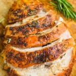 turkey breast that has been cooked and is cut up sitting on a cutting board with orange slices and rosemary sprigs