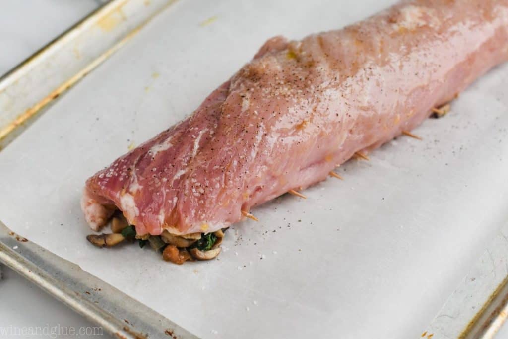 a stuffed pork tenderloin that is on a parchment paper lined baking sheet and ready for the oven