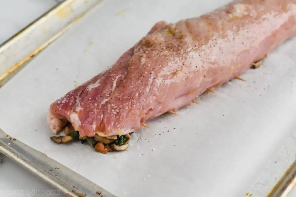 a stuffed pork tenderloin that is on a parchment paper lined baking sheet and ready for the oven
