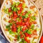 overhead view of blt dip in an oval ceramic baking dish on a wood board with round crackers around it