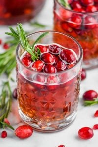 tumbler with christmas sangria in it, garnished with fresh cranberries and a sprig of rosemary