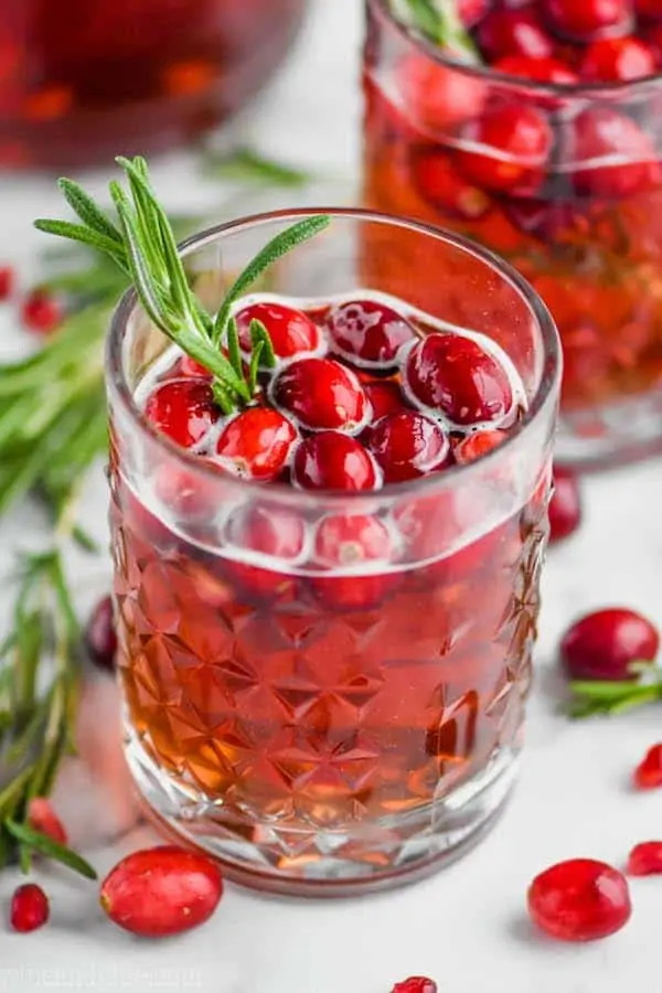 tumbler with christmas sangria in it, garnished with fresh cranberries and a sprig of rosemary