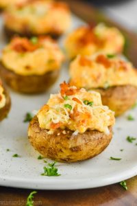 picture of stuffed mushrooms with cream cheese, fresh parsley, and fresh parmesan, with more in the background