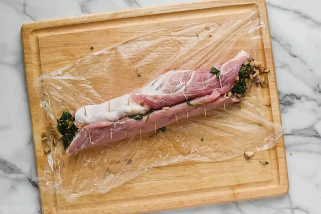 a pork tenderloin that has been stuffed, rolled up, and is being held together with tooth picks before being roasted