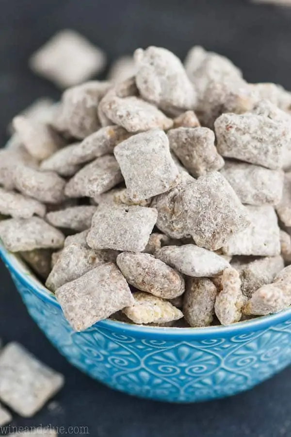 a blue detailed bowl against a dark surface overflowing with a puppy chow recipe