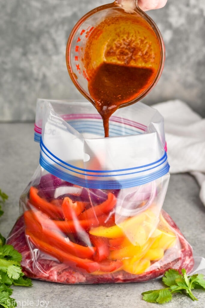 Photo of a bag of vegetables with a hand pouring marinade into bag for Steak Fajitas recipe.