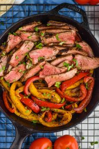 close up of cooked steak sliced thin with sliced peppers in a cast iron skillet, seasoned with fajita marinade