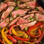 close up of cooked steak sliced thin with sliced peppers in a cast iron skillet, seasoned with fajita marinade