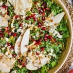 overhead view of a bowl of kale, pomegranate seeds, blue cheese, pine nuts, and pear slices for a winter kale salad