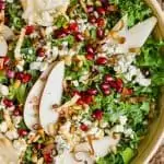 overhead view of a bowl of kale, pomegranate seeds, blue cheese, pine nuts, and pear slices for a winter kale salad