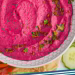pinterest graphic of overhead view of a white bowl full of bright pink beet hummus garnished with fresh parsley, says: beet hummus simplejoy.com