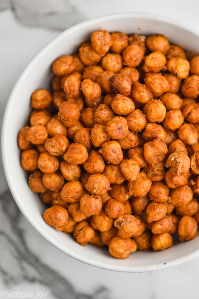 overhead view of a white bowl on a marble countertop full of roasted chickpeas