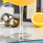 pinterest graphic a sidecar drink in a coupe glass rimmed with sugar with a lemon twist hanging off the side, a bottle of cointreau, half a lemon, and a cocktail shaker in the background, says "sidecar cocktail, simplejoy.com"