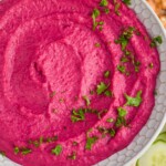 overhead view of a white bowl full of bright pink beet hummus garnished with fresh parsley - 7