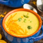 small blue ceramic soup bowl full of broccoli cheddar soup garnished with more cheese and round orange crackers next to the bowl - 17