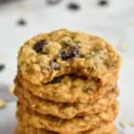 stack of oatmeal raisin cookies on a marble countertop with more on a cooling rack in the background