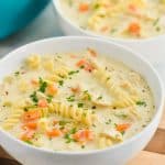 a small white bowl of creamy chicken noodle soup on a cutting board with another bowl behind, both garnished with fresh parsley - 21