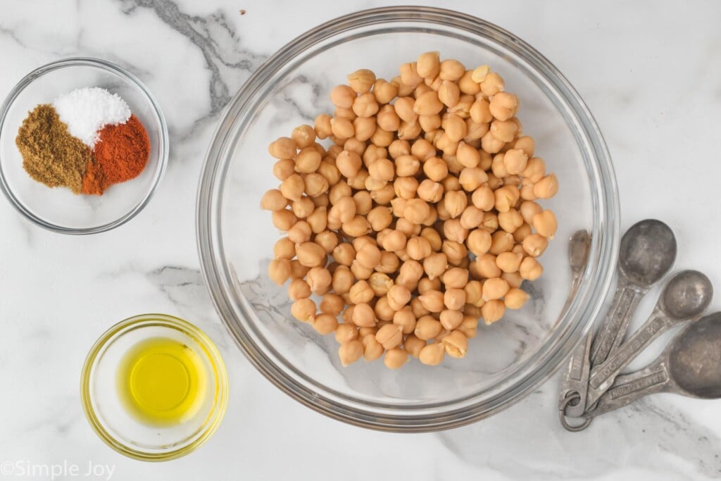 overhead view of drained and rinsed chickpeas in a bowl next to oil and spices