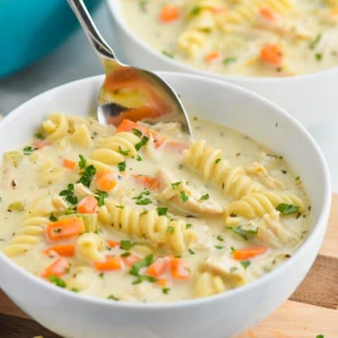 a white bowl full of the best creamy chicken noodle soup recipe with a spoon dipping in