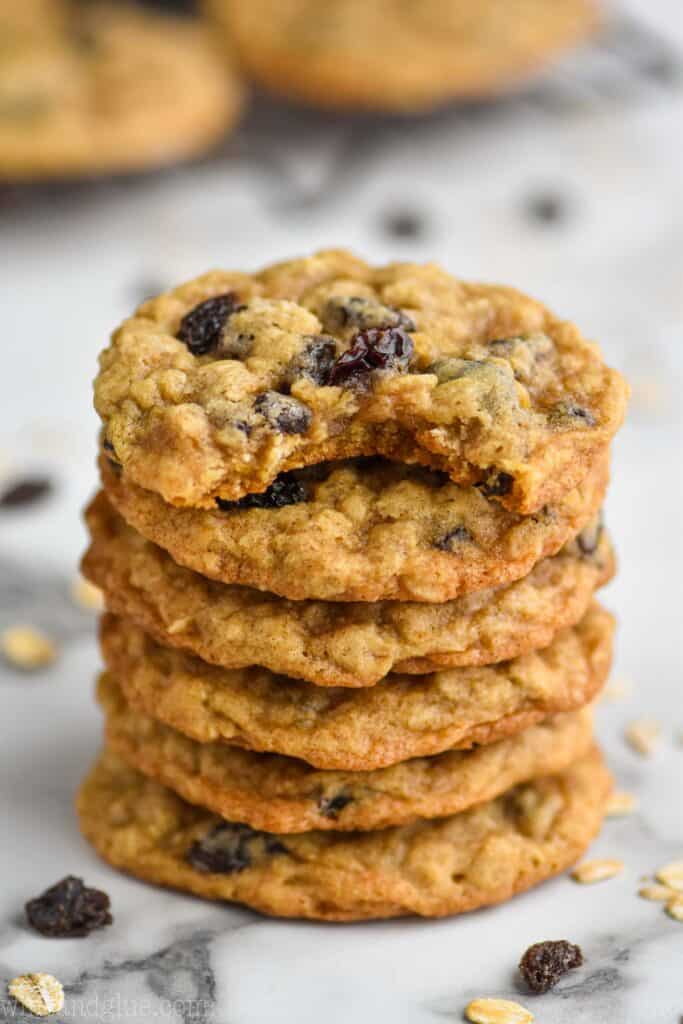 stack of oatmeal raisin cookies on a marble countertop with more on a cooling rack in the background
