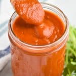 a spoon dishing up red enchilada sauce recipe as it slowly drips off back into mason jar