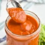 a spoon dishing up red enchilada sauce recipe as it slowly drips off back into mason jar