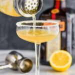 a cocktail shaker pouring a sidecar cocktail into a coupe glass rimmed with sugar - 7