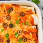 overhead of beef enchiladas in a ceramic baking dish, garnished with black olives and cilantro