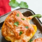 a half yellow bell pepper that is a chicken fajita stuffed pepper topped with bubbly brown cheese on an old baking sheet and garnished with cilantro