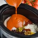 a crockpot with ingredients for enchilada soup and homemade enchilada sauce being poured into it