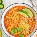 overhead view of enchilada soup in a white bowl garnished with chip strips, lime wedges, cilantro, and shredded cheese - 13