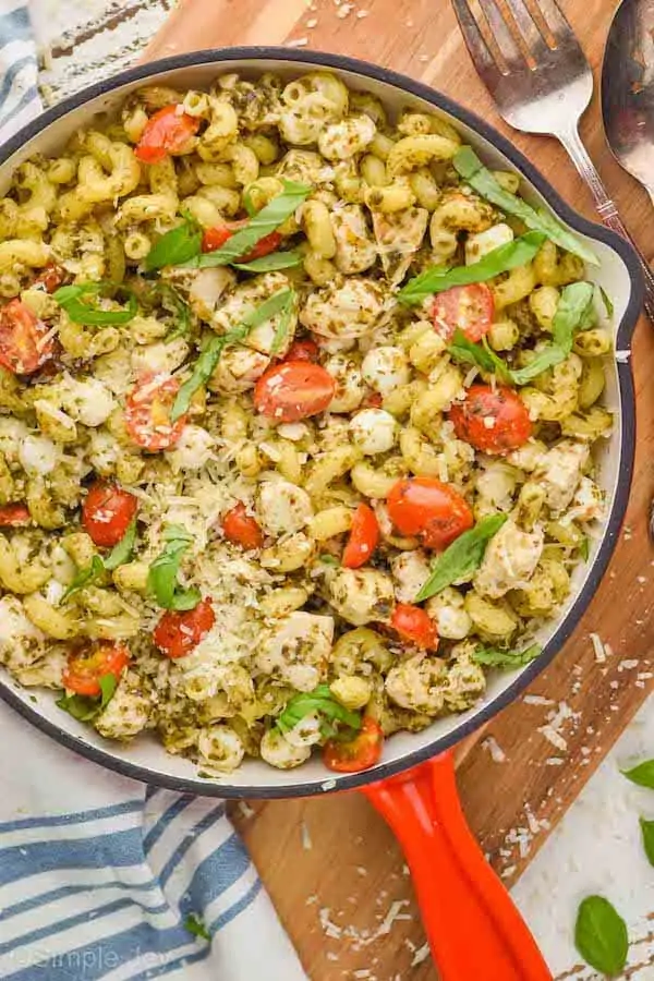 overhead photo of a skillet with a red handle holding an easy skillet chicken pesto pasta recipe, garnished with fresh Parmesan and fresh basil