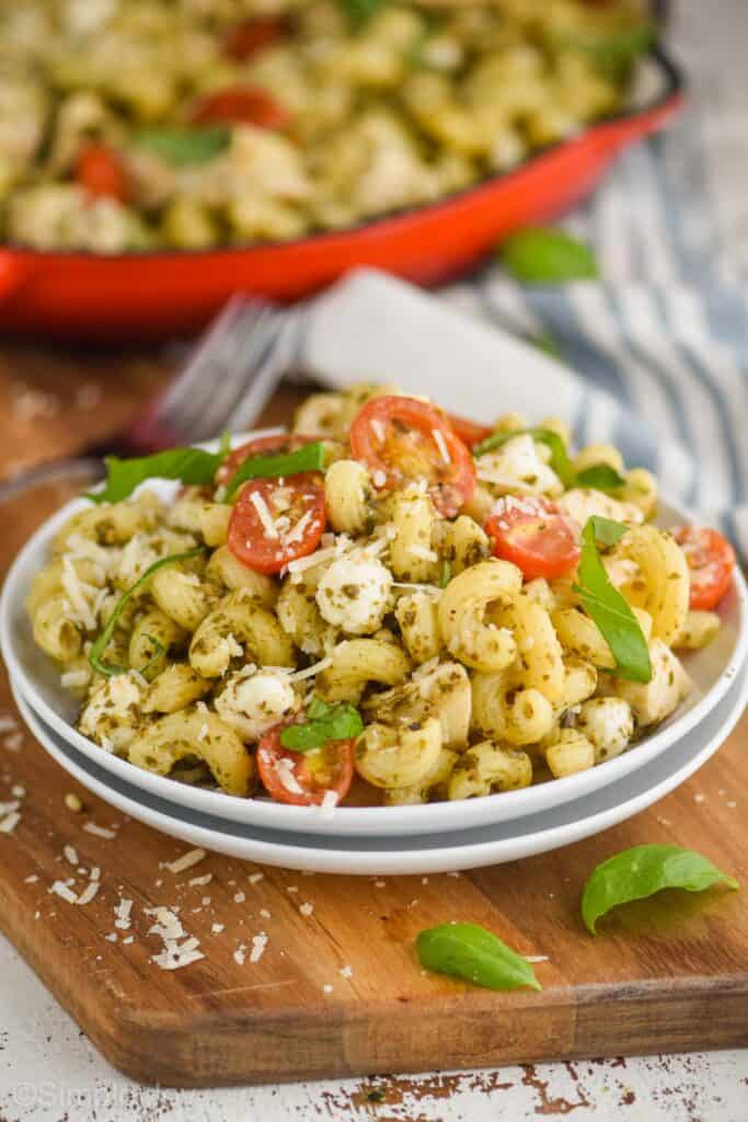 two small plates stacked with chicken pesto pasta on it, cavatapi noodles, small tomatoes, fresh basil, and small mozzarella pearls