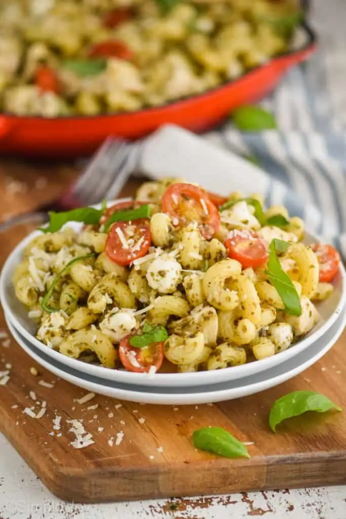 two small plates stacked with chicken pesto pasta on it, cavatapi noodles, small tomatoes, fresh basil, and small mozzarella pearls