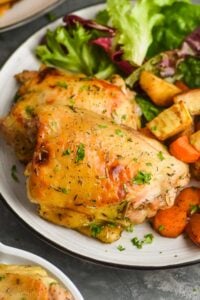close up of baked chicken thighs on a plate with lettuce and roasted root vegetables