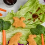 a piece of iceberg lettuce serves as the background for a dinosaur scene made out of veggies and dinosaur chicken nuggets