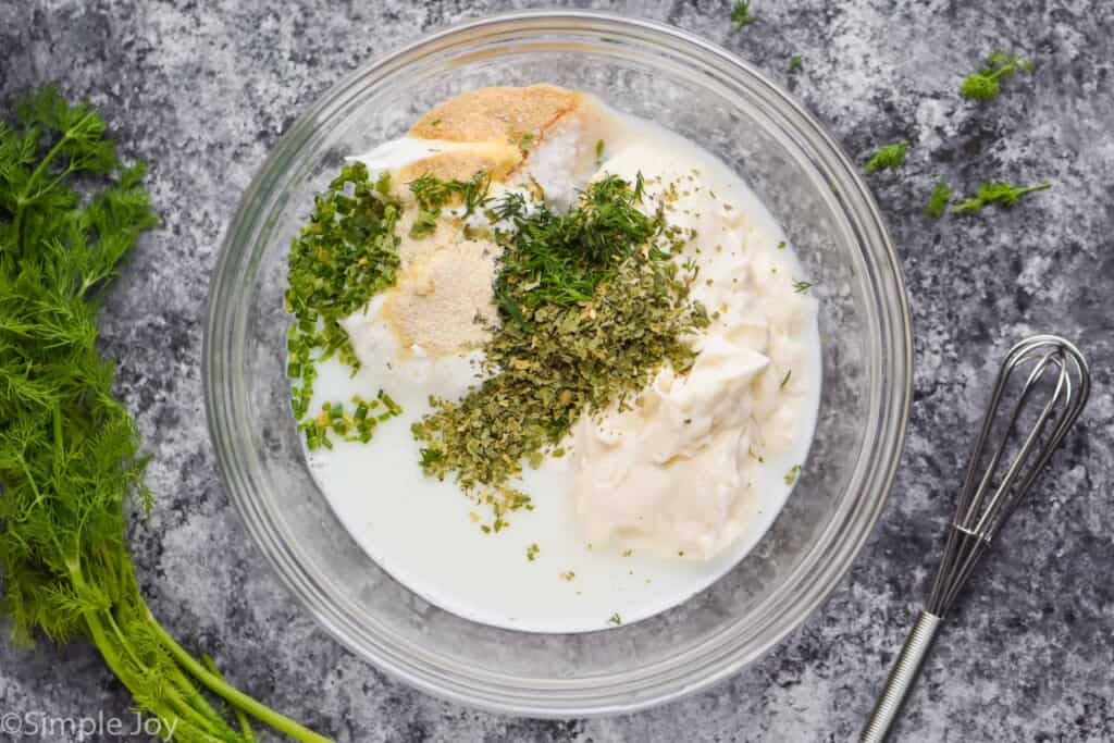 overhead of a bowl of ranch dressing ingredients with fresh dill next to it and a small whisk