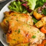close up of baked chicken thighs on a plate with lettuce and roasted root vegetables