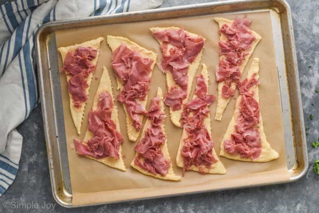 overhead of a baking sheet with 8 crescent roll triangles covered in corned beef