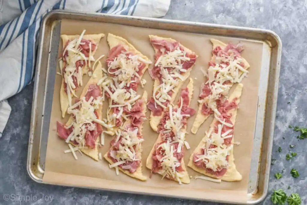 overhead of a baking sheet with with 8 unrolled crescent rolls with corned beef, Swiss cheese, and sauerkraut