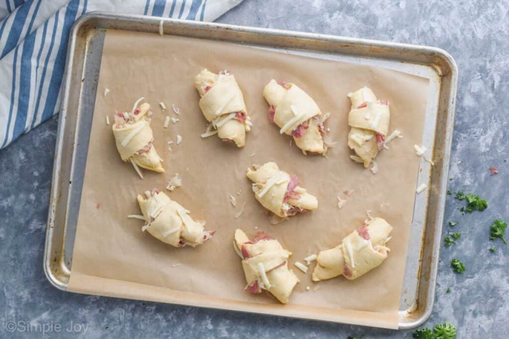 overhead of a baking sheet with parchment paper and 8 reuben crescent rolls waiting to be baked